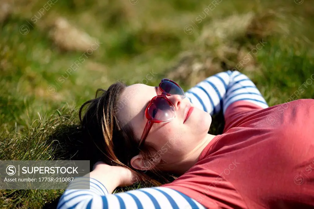 Young woman wearing heart shape sunglasses lying on grass