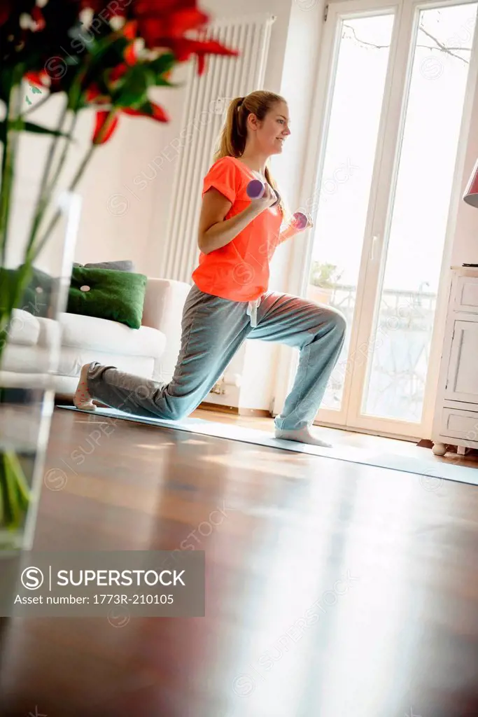 Young woman exercising with dumb-bells at home