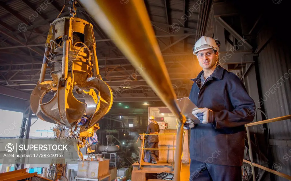 Portrait of steel worker overseeing mechanical grabber in steel foundry