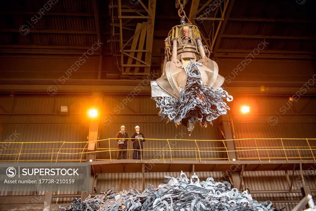 Steel workers watching mechanical grabber in steel foundry