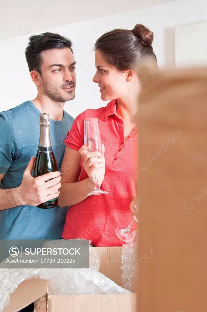 Young couple celebrating with champagne amongst cardboard boxes