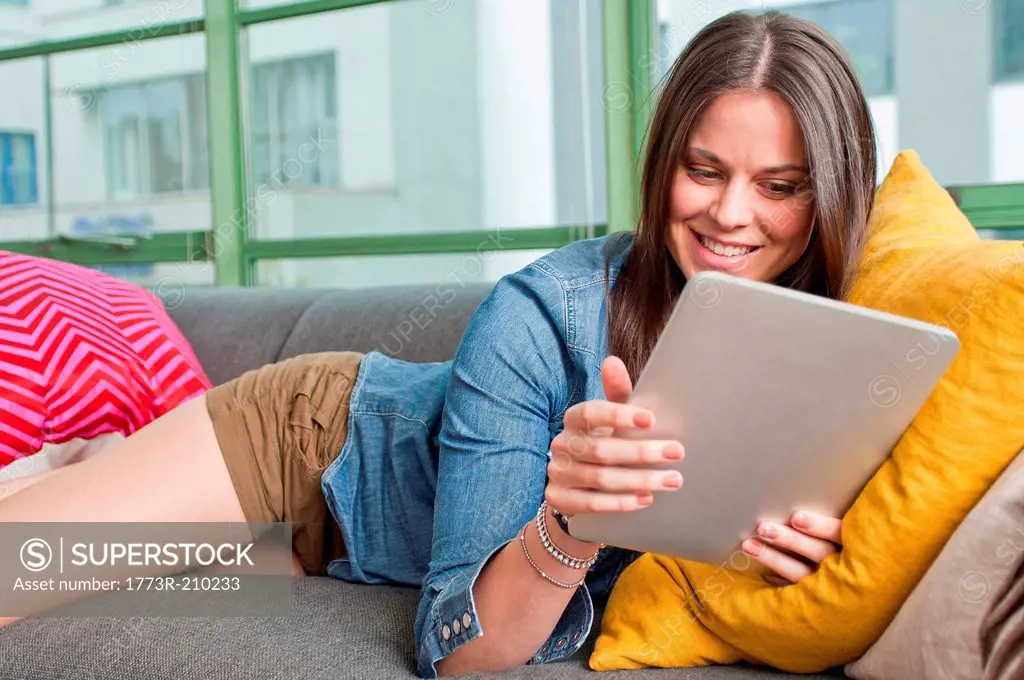 Young woman lying on sofa holding digital tablet