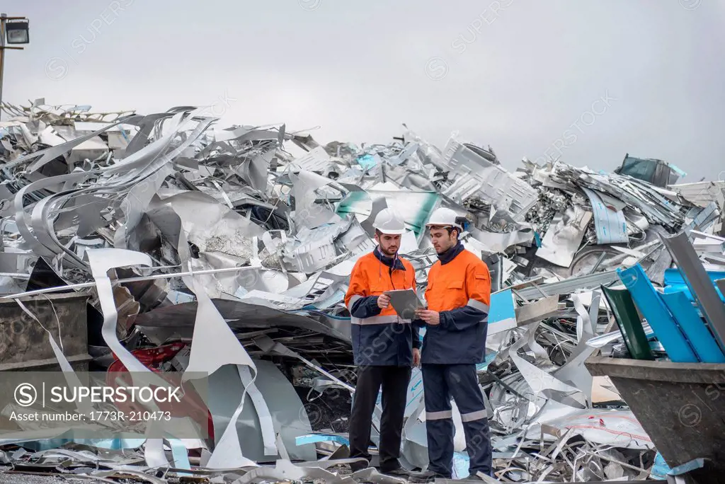 Two workers looking at clip board in front of scrap aluminum