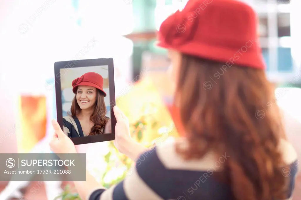 Woman in burgundy hat taking self portrait on digital tablet