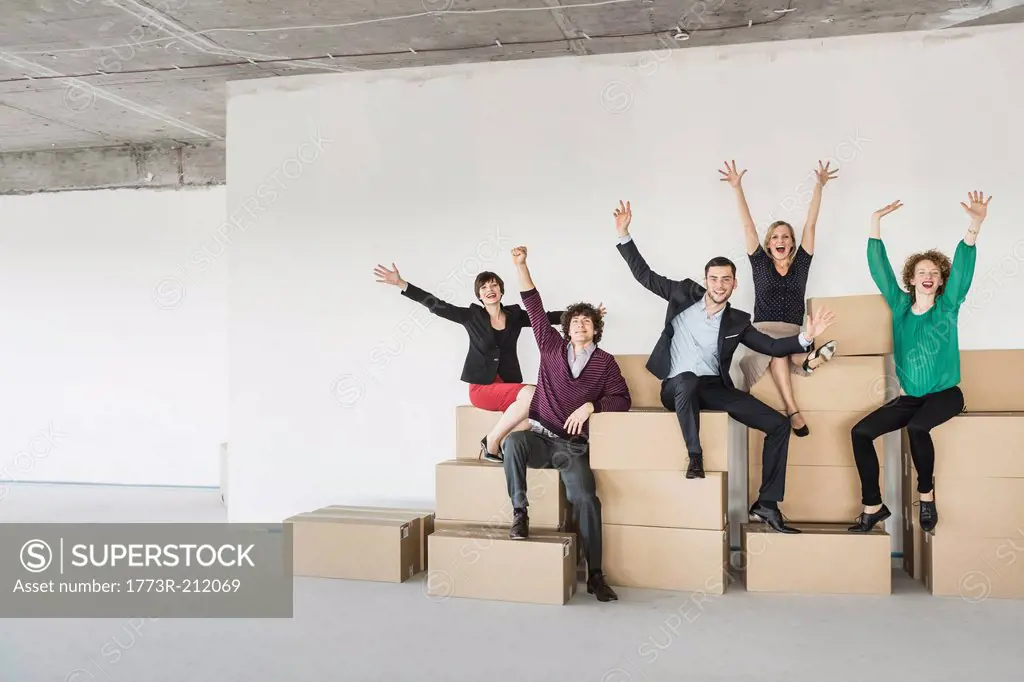 Businesspeople sitting on pile of cardboard boxes with arms raised