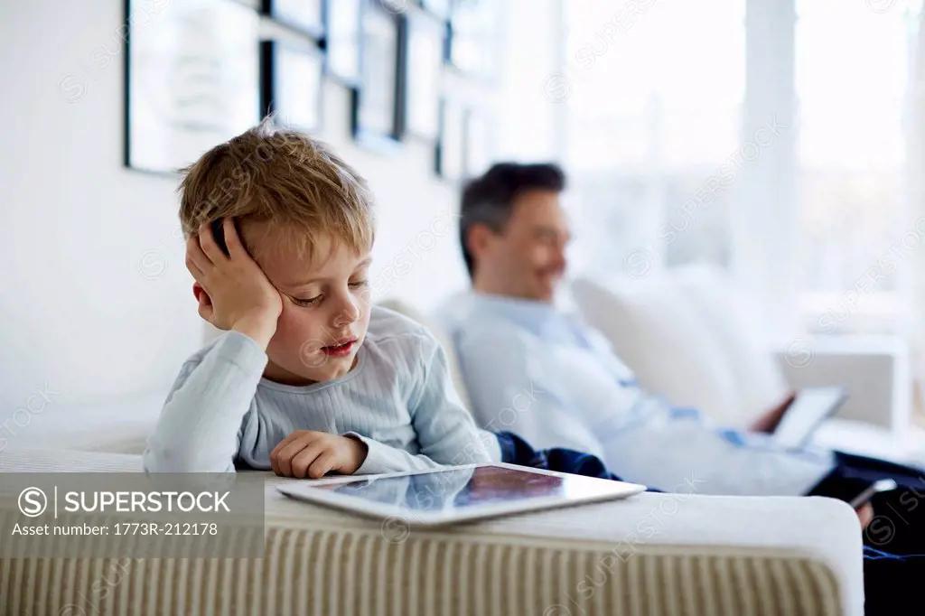 Father and son sitting on sofa using digital tablets