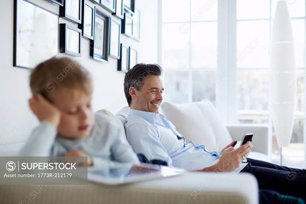 Father and son sitting on sofa using digital tablet and smartphone