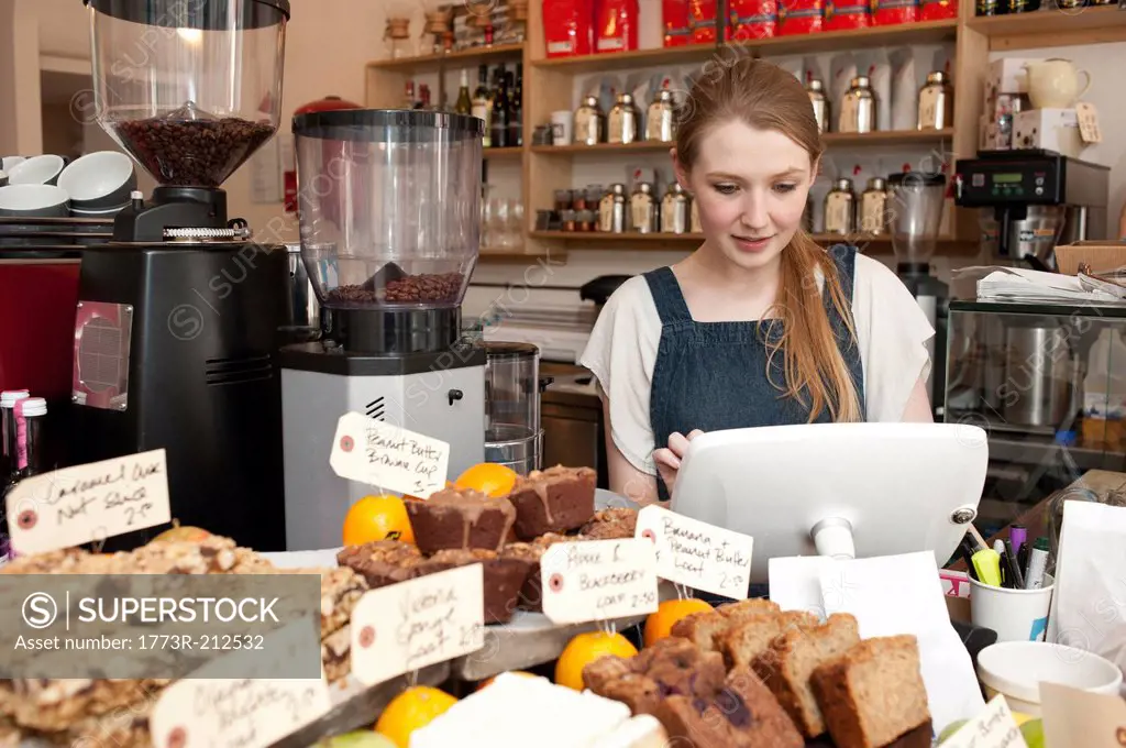 Young woman using cash register in cafe