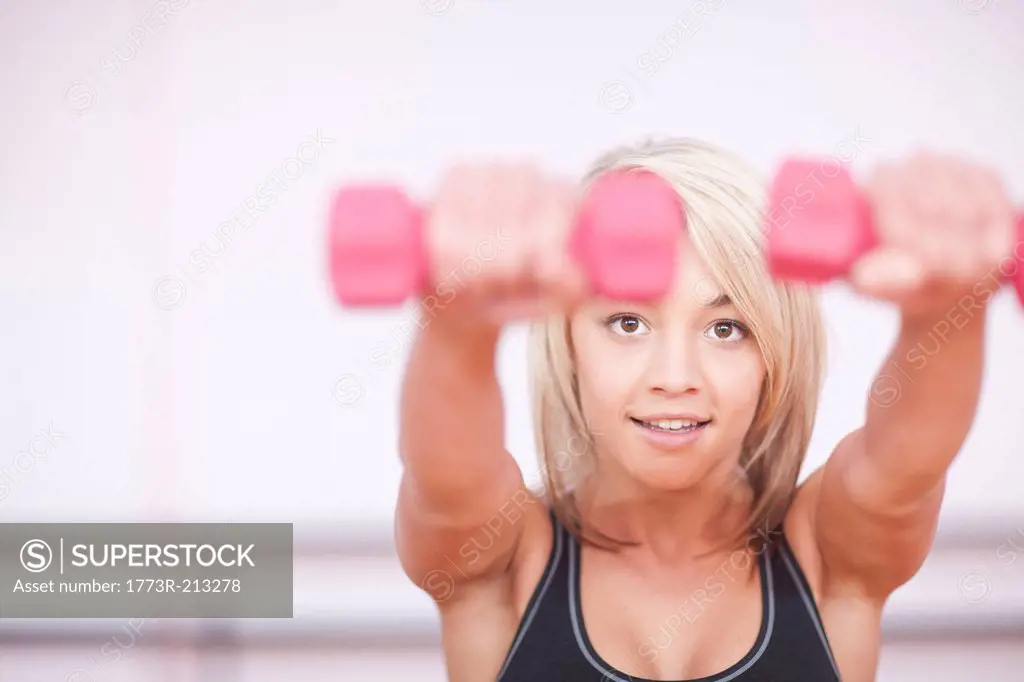 Portrait of young woman training with dumbbells in gym