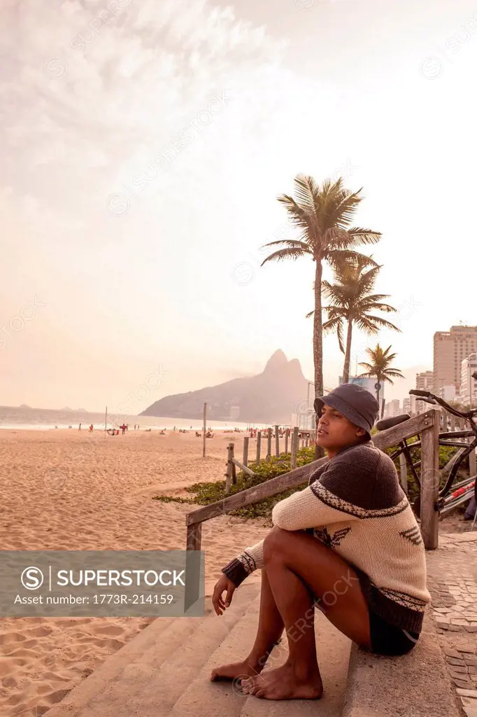 Young man sitting on steps on Ipanema Beach, Rio de Janeiro, Brazil