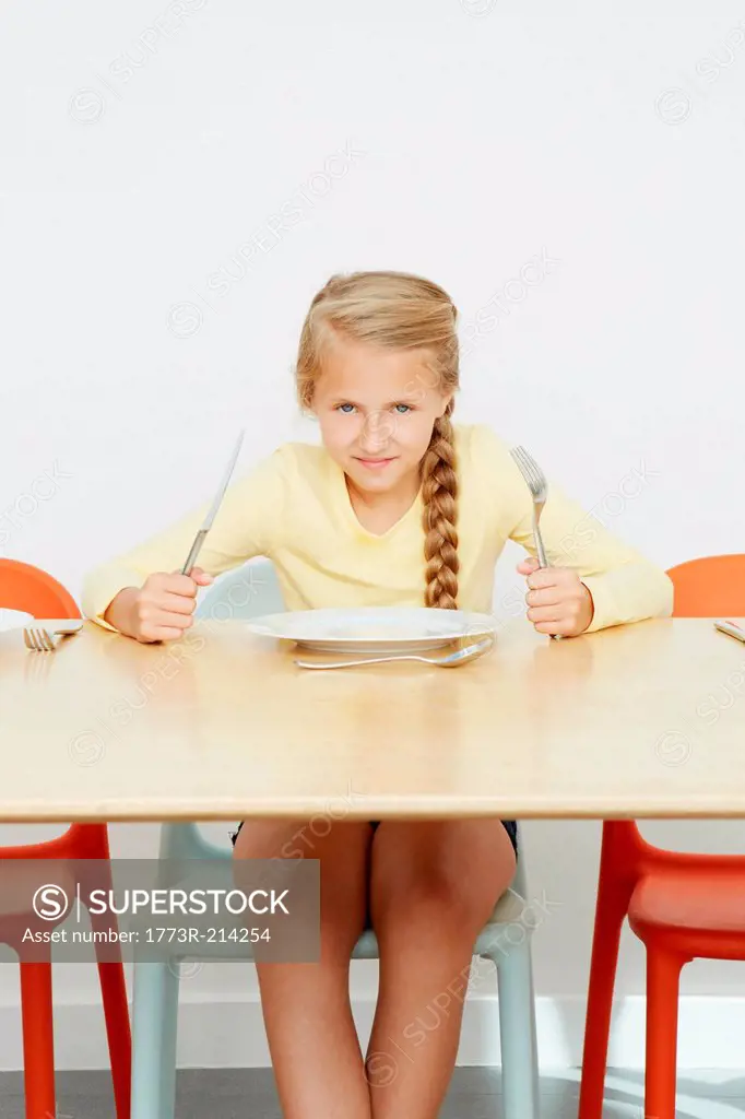 Girl sitting at table with empty plate holding cutlery