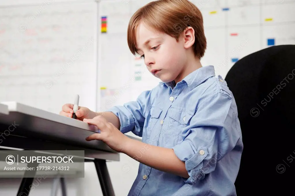 Boy writing at desk in office