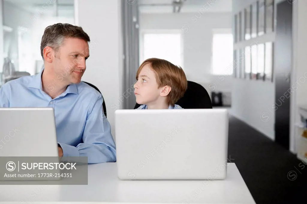 Father and son using laptops, face to face