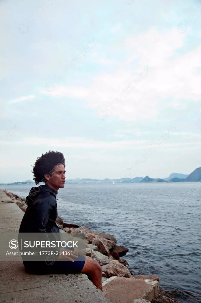 Young man sitting on wall looking at sea, Rio de Janeiro, Brazil