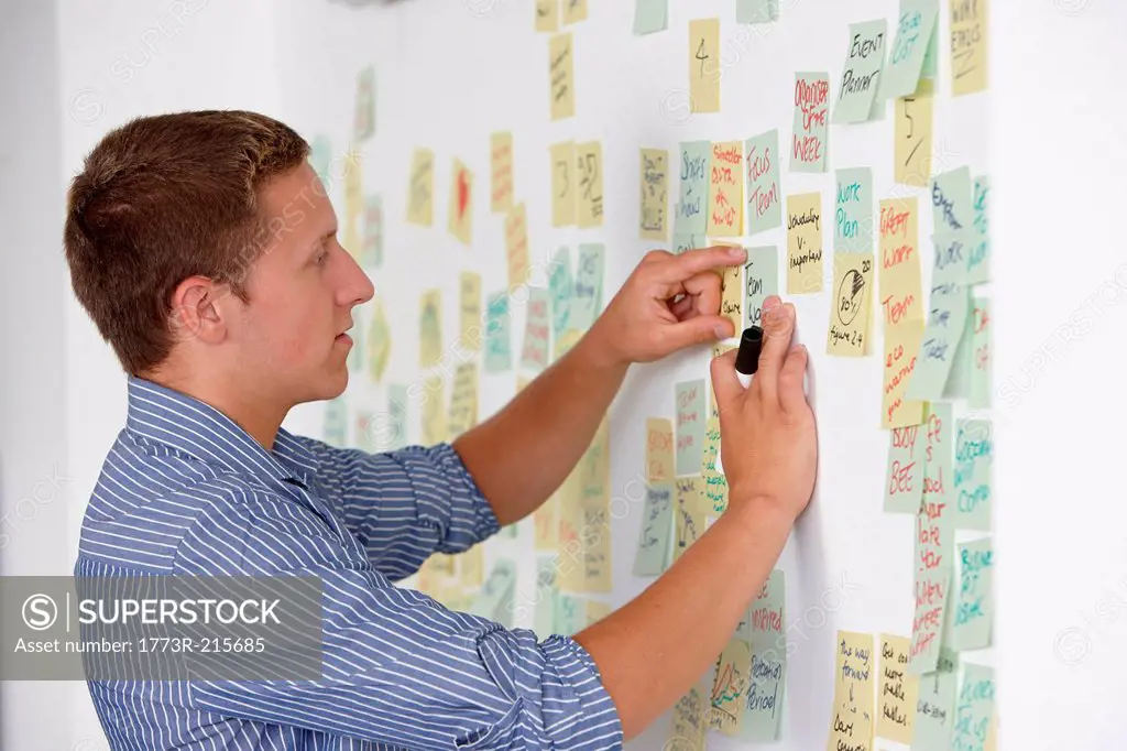 Young man sticking adhesive note on wall