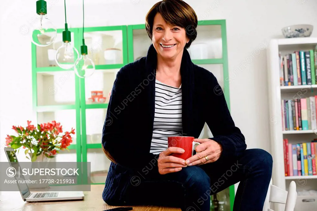 Senior woman sitting on desk holding mug