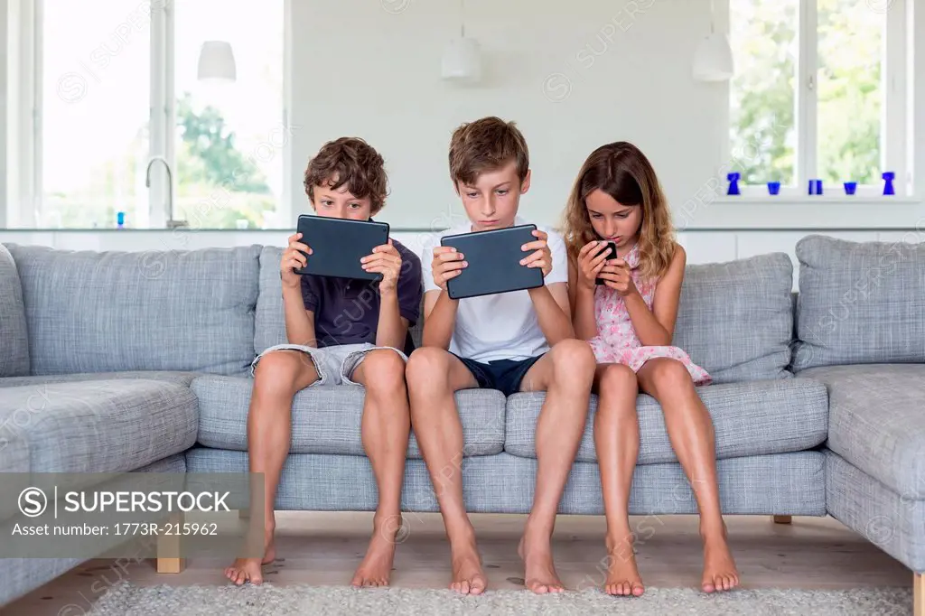 Brothers and sister on sofa with digital tablets and mobile