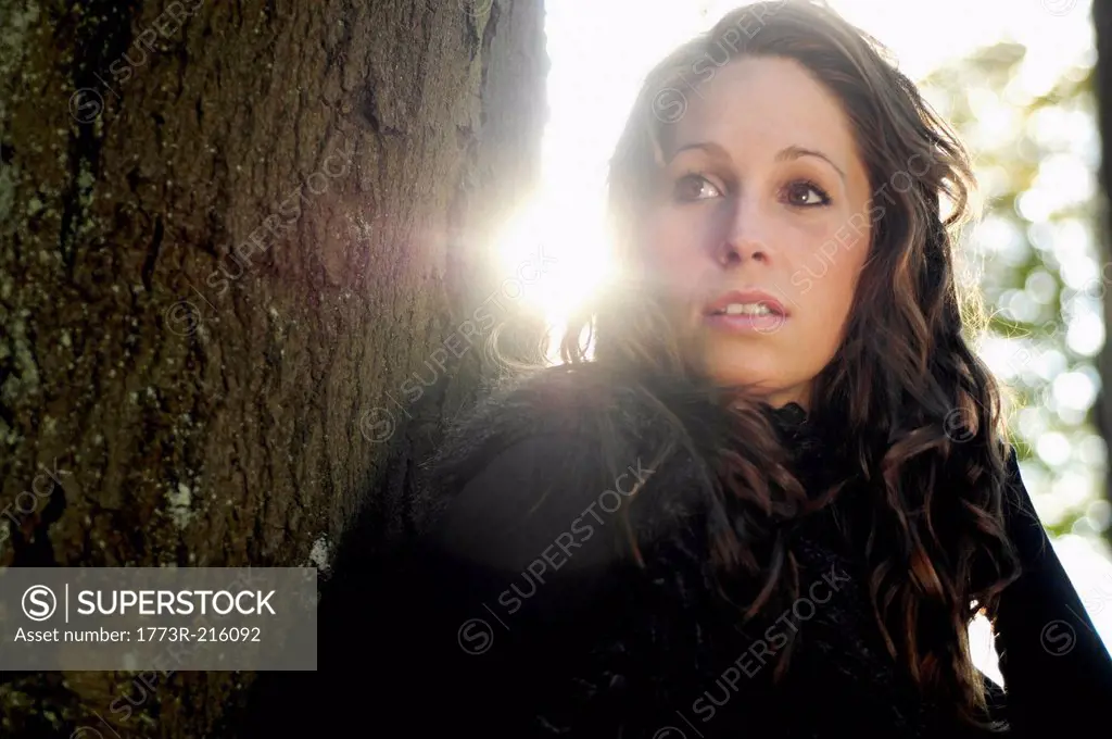 Portrait of young woman by tree trunk in autumn