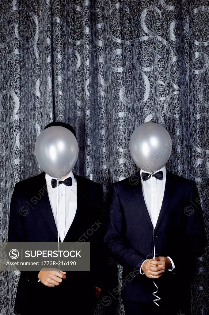 Portrait of two young men with balloons in front of faces