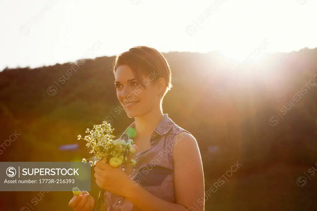 Young woman in meadow with bunch of wild flowers