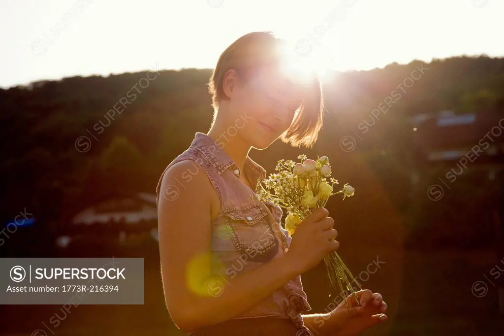 Young woman in meadow holding bunch of wild flowers