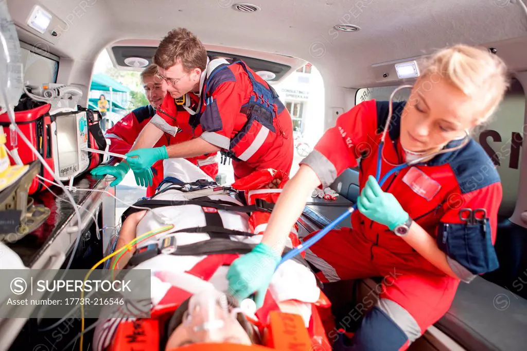 Paramedics using stethoscope on patient in ambulance