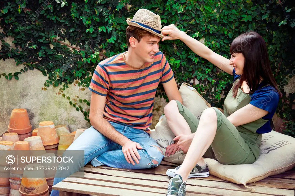 Couple sitting on wooden palettes, man wearing straw hat