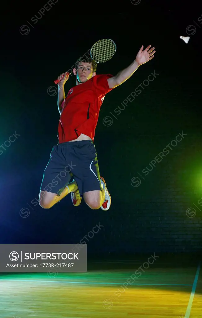Young male badminton player mid air on court