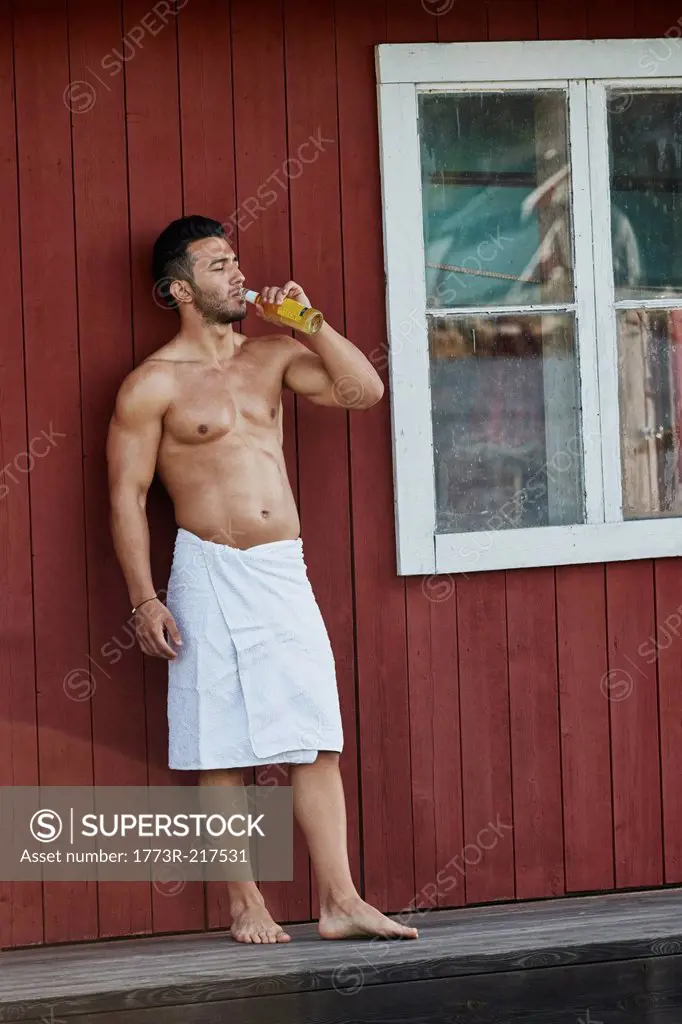 Young man drinking a beer outside sauna