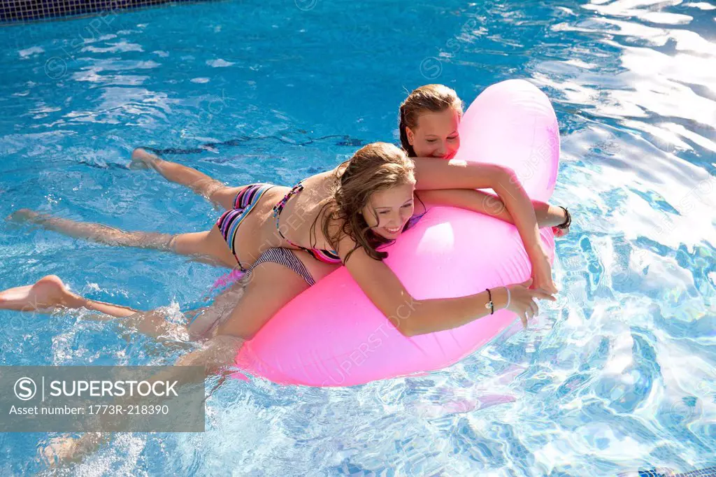 Two teenage girls holding onto air bed in swimming pool