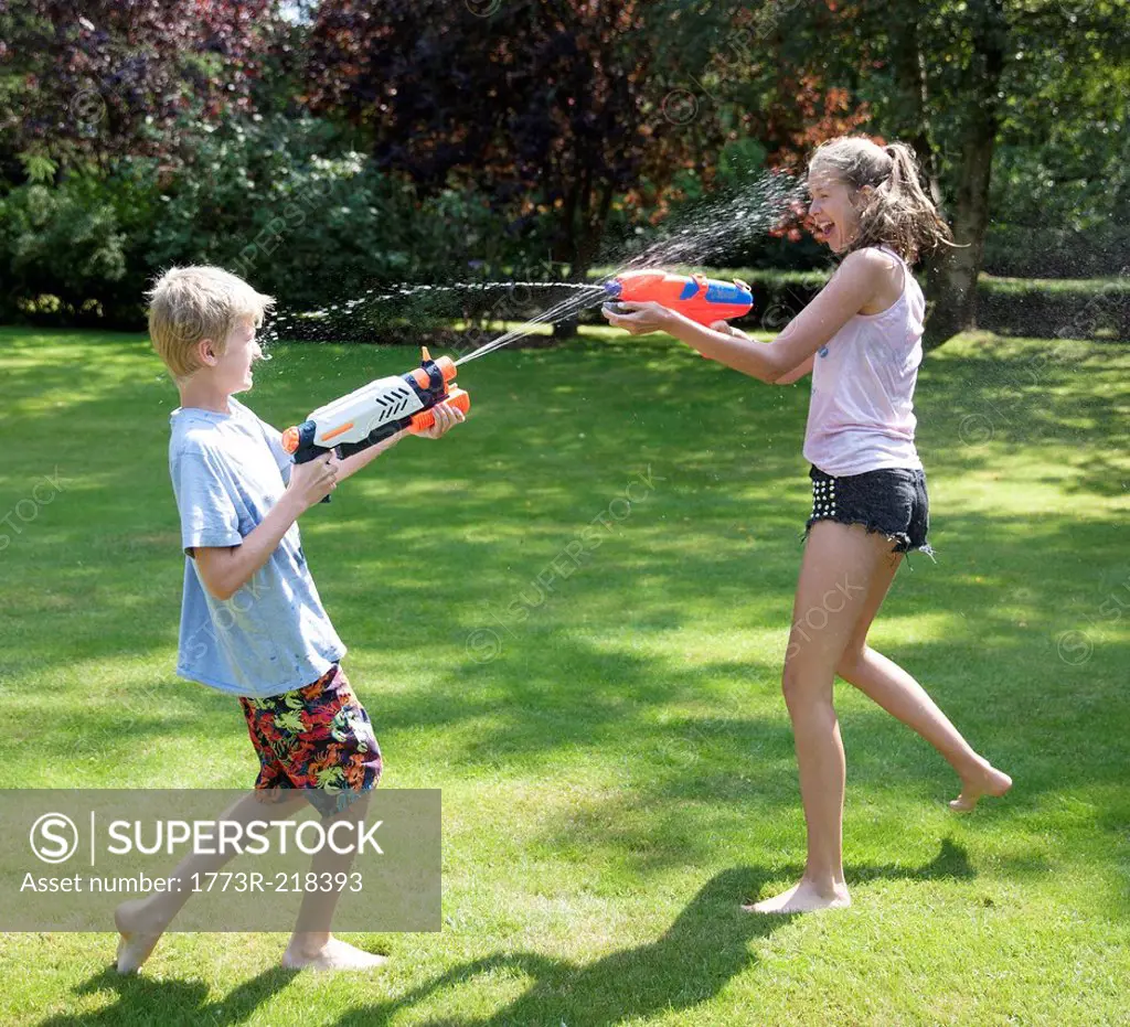 Brother and sister play fighting with water guns in garden