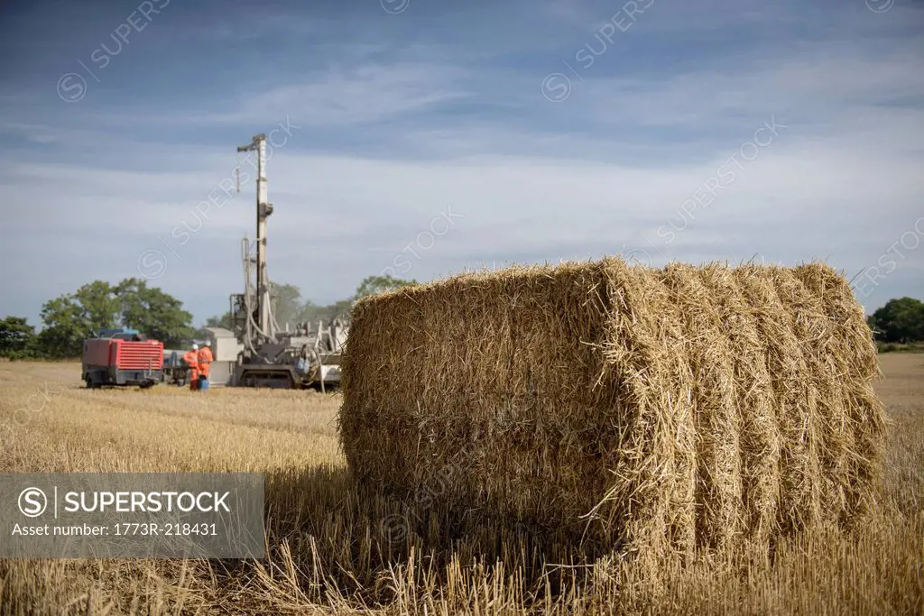 Drilling rig in field with hay bale in foreground
