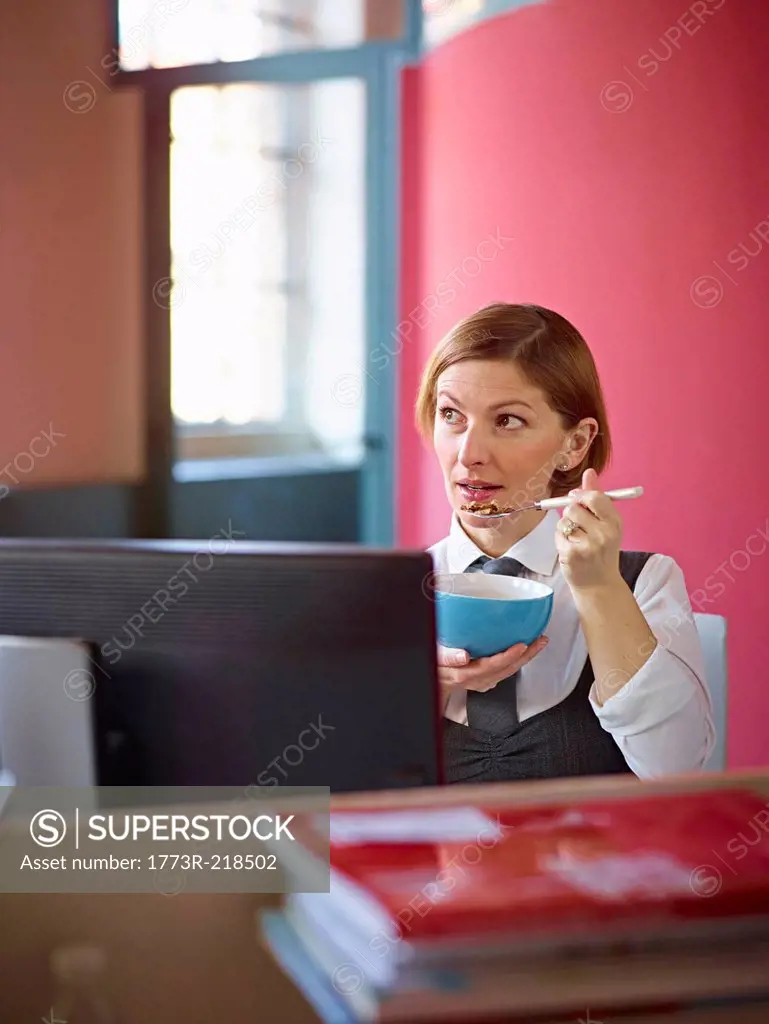 Office worker eating breakfast cereal at desk