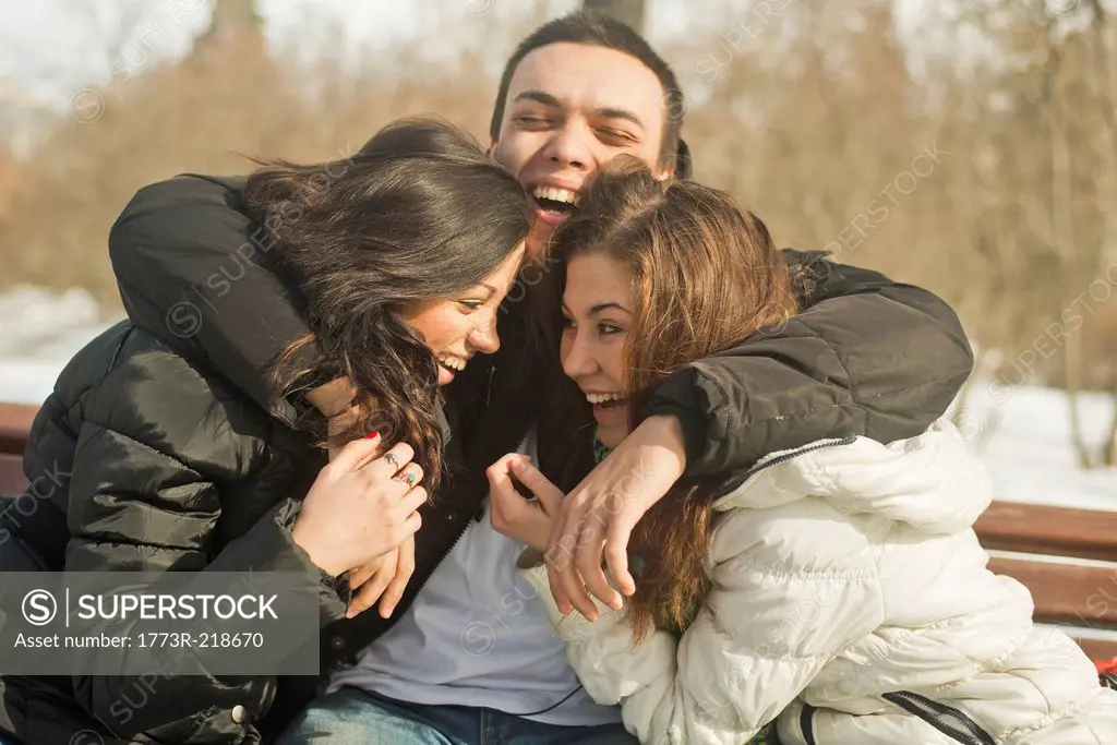 Three young adults hugging on park bench in winter