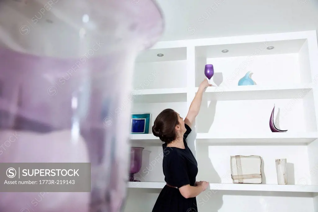 Young woman reaching for wine glass on shelf in living room