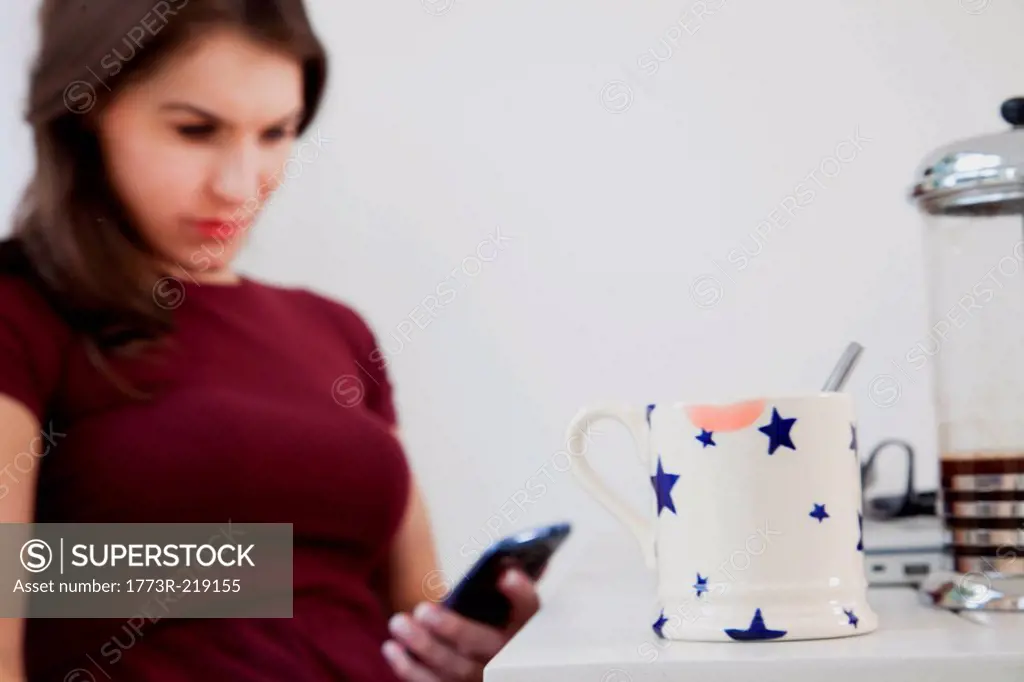 Young woman using cell phone with coffee mug in foreground