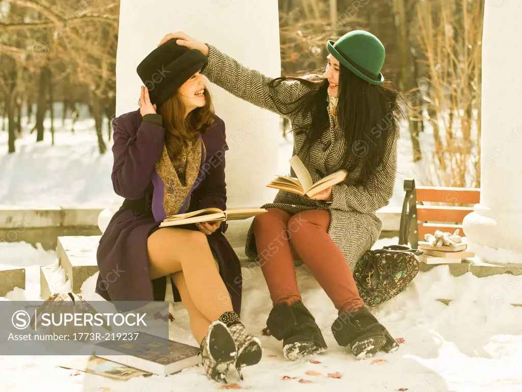 Two young women with books on park bench in snow