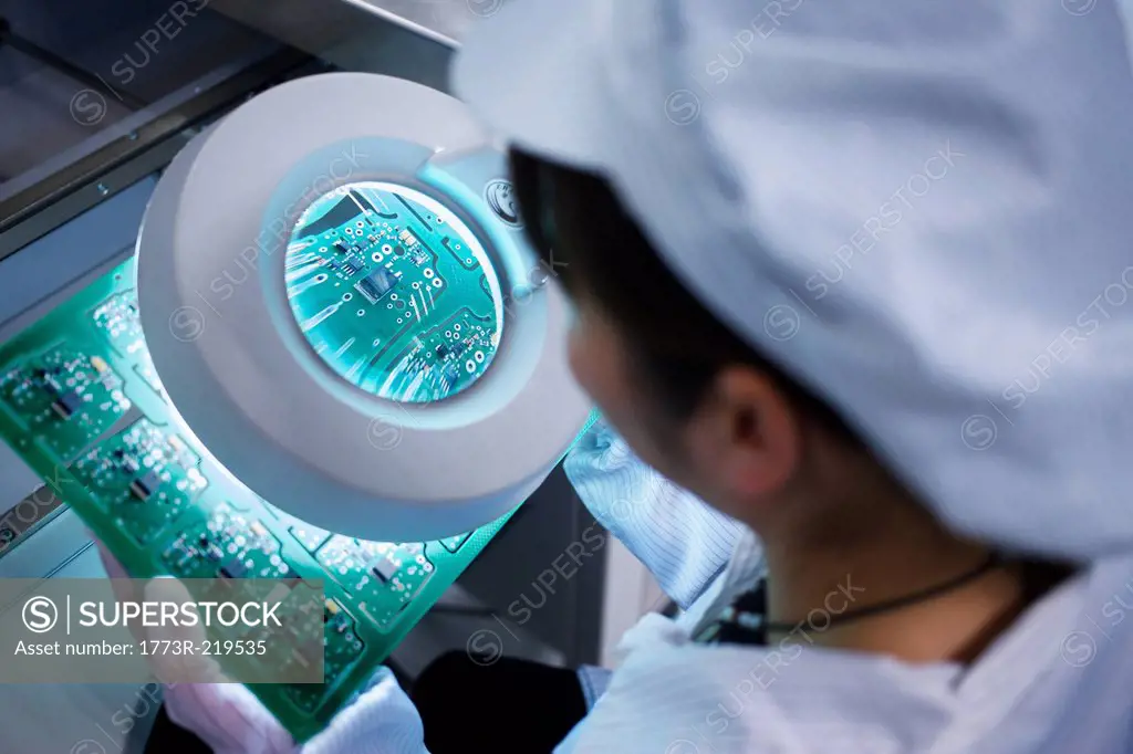 Worker at small parts manufacturing factory in China looking through magnifier at microchips
