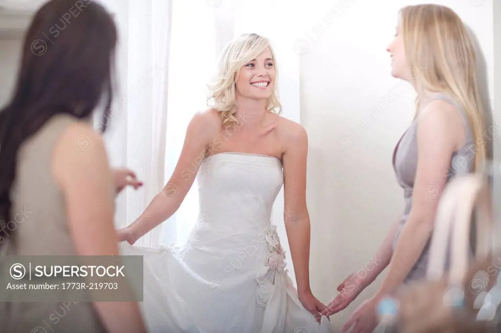 Young woman trying on wedding dress, with friends