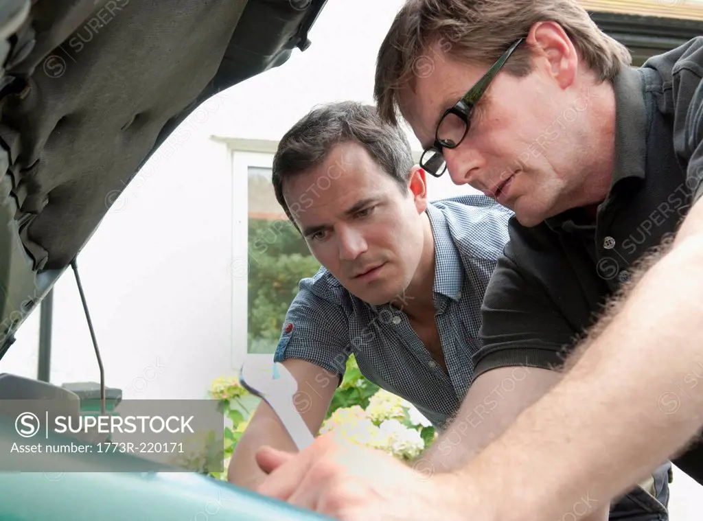 Two male adult friends checking under car hood