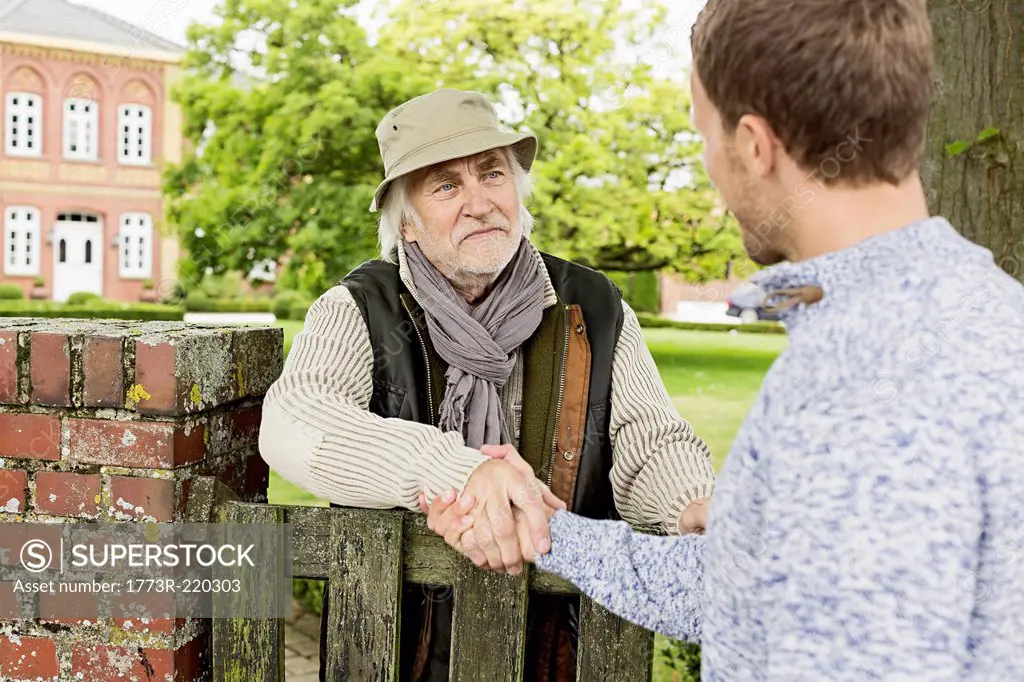 Senior man and mid adult man shaking hands over gate