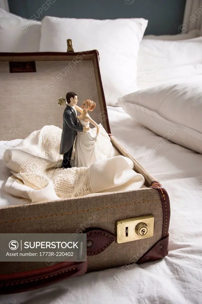 Open suitcase on bed with wedding figurines