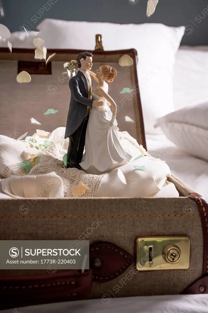 Open suitcase on bed with wedding figurines and confetti