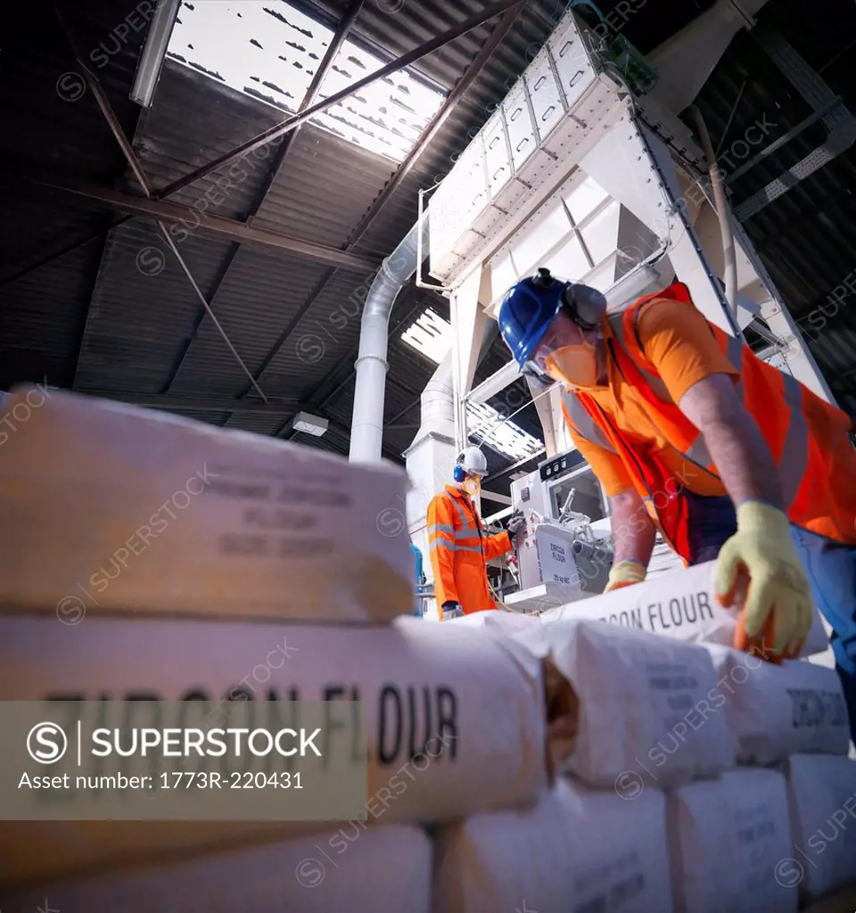 Workers in protective clothing filling zircon flour bags in mill, low angle view