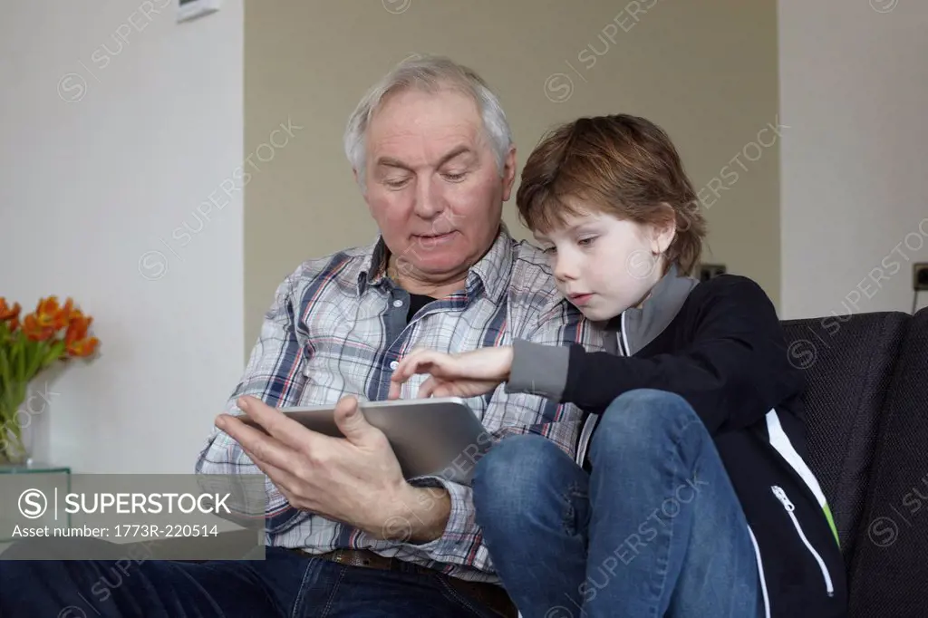 Senior man with grandson at home using digital tablet