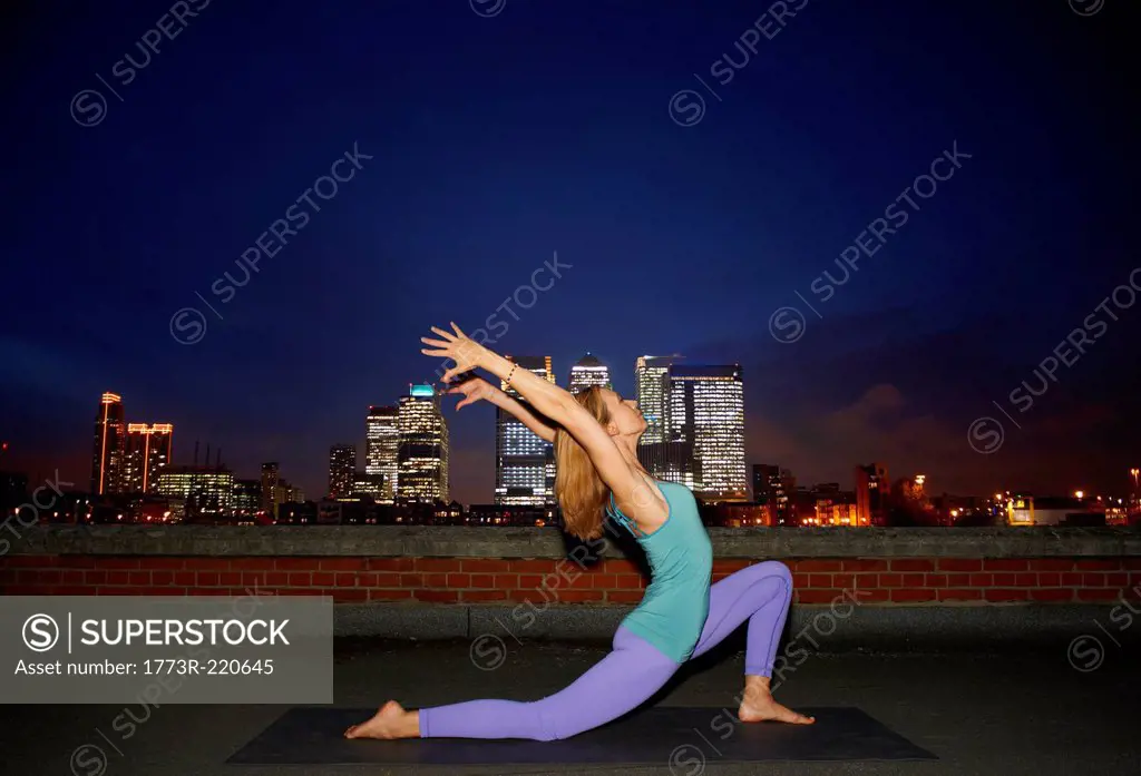 Mid adult woman doing yoga on city rooftop at night