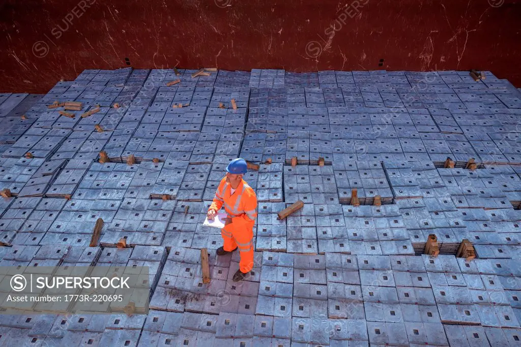 Worker in reflective workwear standing on metal alloy cargo in ship's hold