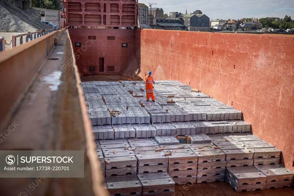 Worker standing on metal ingots in ship's hold