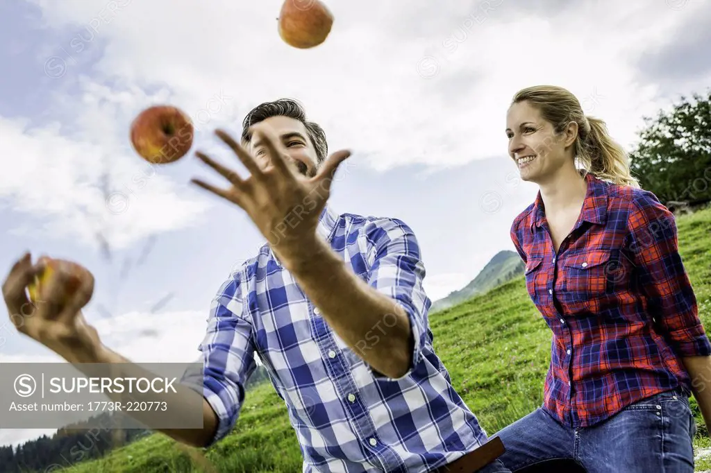 Woman looking at man juggling apples