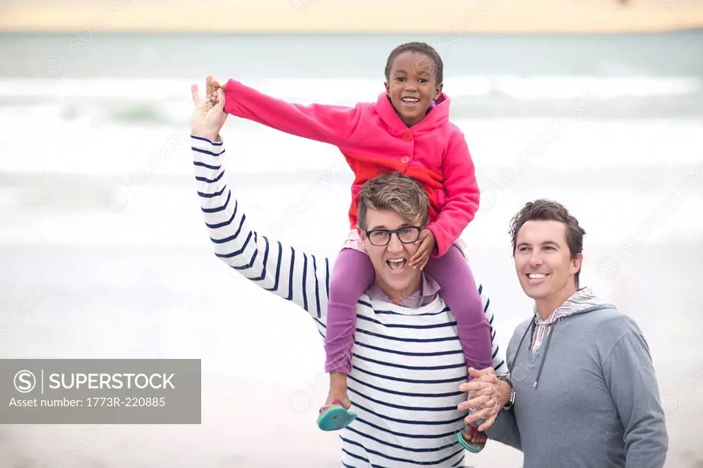 Gay couple walking on beach with child on shoulders